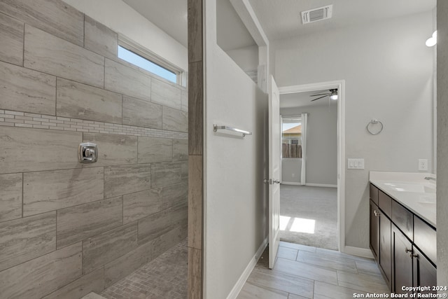 bathroom with a tile shower, vanity, ceiling fan, and plenty of natural light