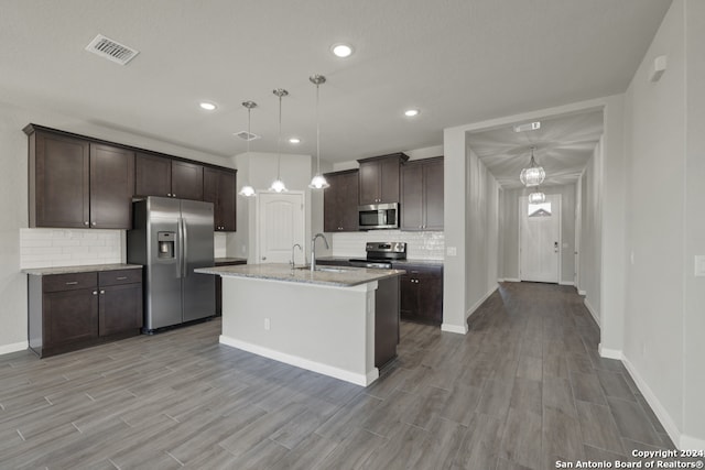 kitchen with an island with sink, hanging light fixtures, sink, light hardwood / wood-style flooring, and appliances with stainless steel finishes