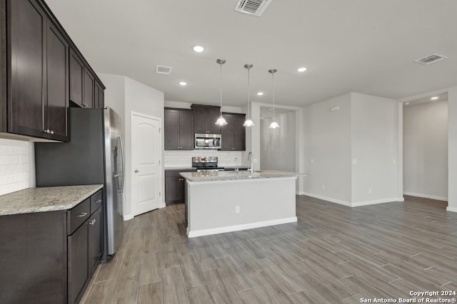 kitchen with light wood-type flooring, appliances with stainless steel finishes, hanging light fixtures, and a kitchen island with sink