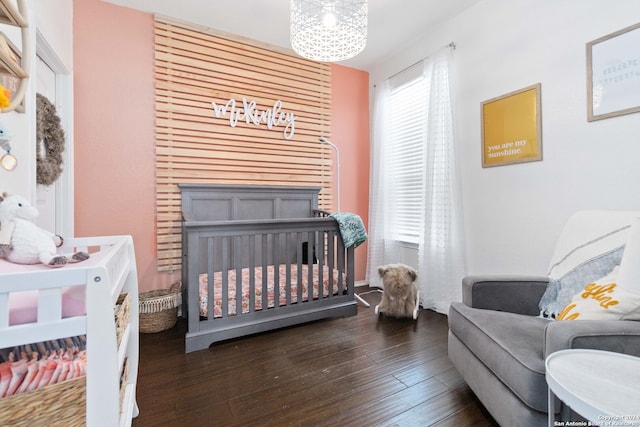 bedroom featuring a chandelier, a nursery area, and dark hardwood / wood-style flooring