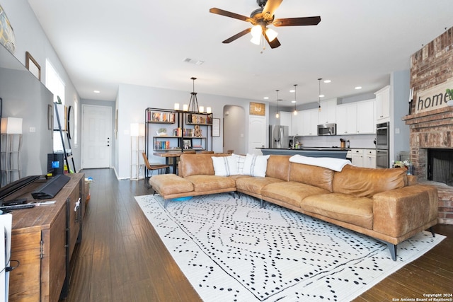 living room featuring ceiling fan with notable chandelier, dark hardwood / wood-style floors, and a brick fireplace