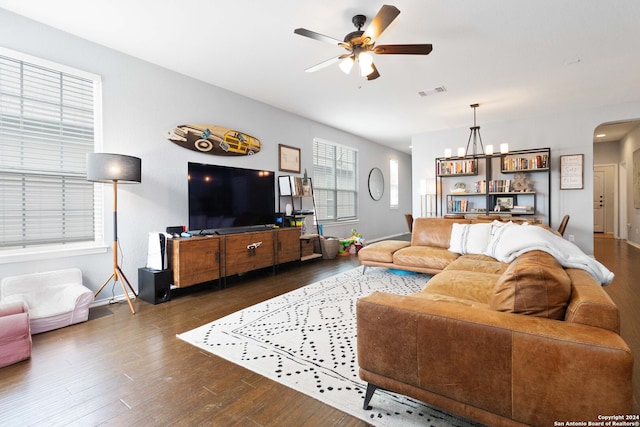 living room featuring ceiling fan with notable chandelier and dark wood-type flooring