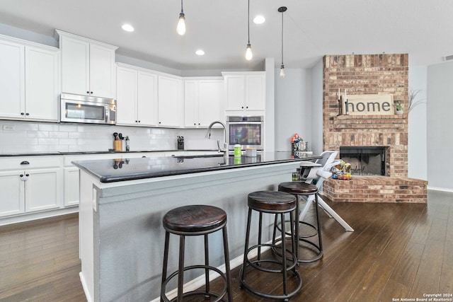 kitchen with white cabinets, decorative light fixtures, dark wood-type flooring, stainless steel appliances, and a fireplace