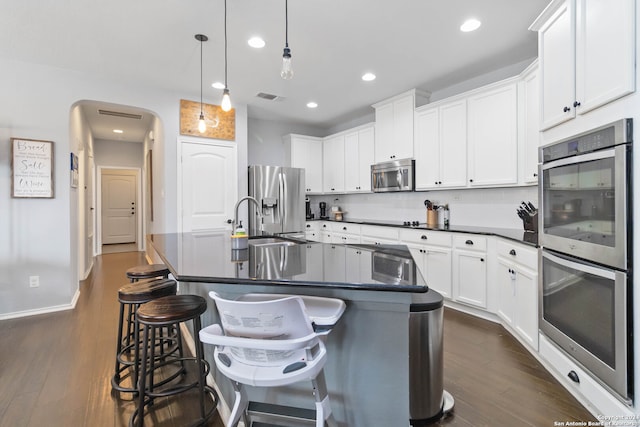 kitchen with a center island with sink, appliances with stainless steel finishes, dark hardwood / wood-style floors, and hanging light fixtures