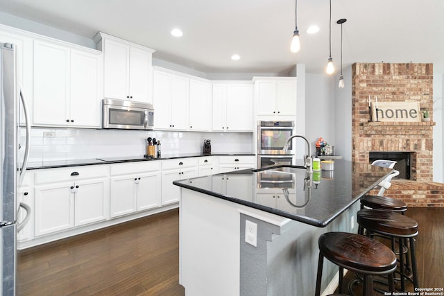 kitchen featuring appliances with stainless steel finishes, backsplash, pendant lighting, a kitchen island with sink, and dark hardwood / wood-style floors