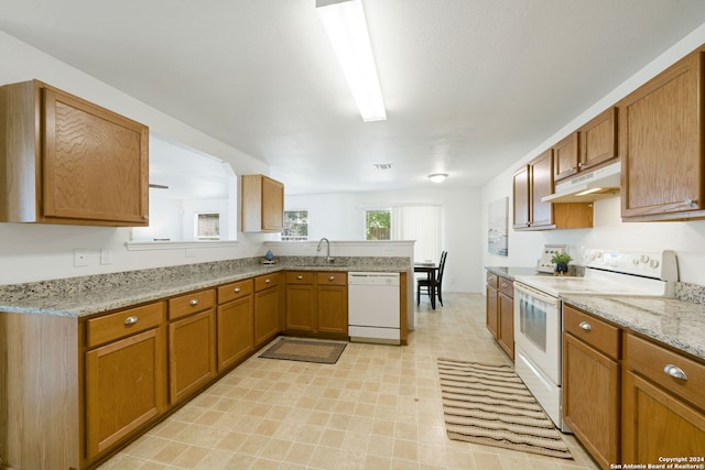 kitchen with light stone counters, kitchen peninsula, sink, and white appliances