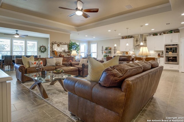 tiled living room featuring ornamental molding, a tray ceiling, and ceiling fan