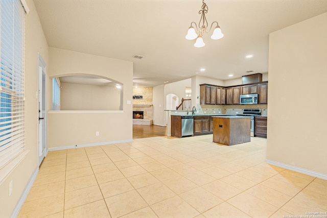 kitchen with a chandelier, a kitchen island, stainless steel appliances, decorative light fixtures, and a large fireplace