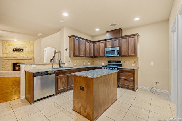 kitchen with light tile patterned flooring, sink, kitchen peninsula, a kitchen island, and appliances with stainless steel finishes