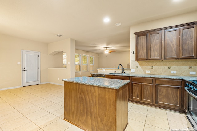 kitchen with light stone counters, sink, tasteful backsplash, a kitchen island, and stainless steel range oven