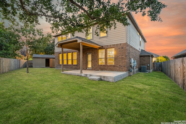 back house at dusk featuring cooling unit, a patio, a lawn, and a storage unit