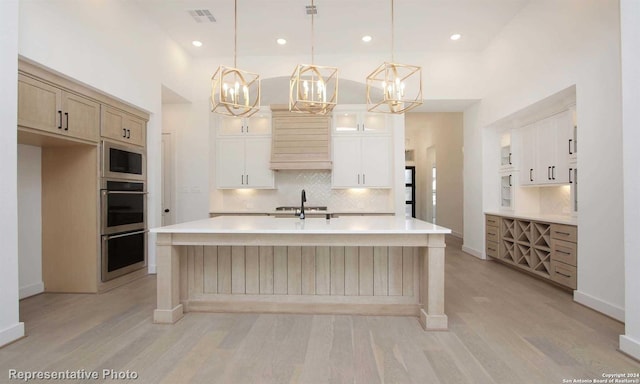 kitchen with hanging light fixtures, tasteful backsplash, light hardwood / wood-style floors, an island with sink, and built in microwave