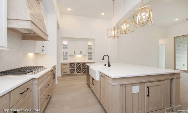 kitchen with decorative light fixtures, sink, custom exhaust hood, stainless steel gas cooktop, and a center island with sink