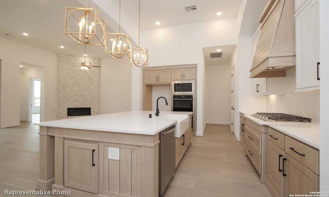 kitchen featuring custom exhaust hood, appliances with stainless steel finishes, an island with sink, pendant lighting, and backsplash