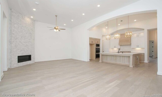 unfurnished living room with a stone fireplace, high vaulted ceiling, ceiling fan, and light hardwood / wood-style flooring