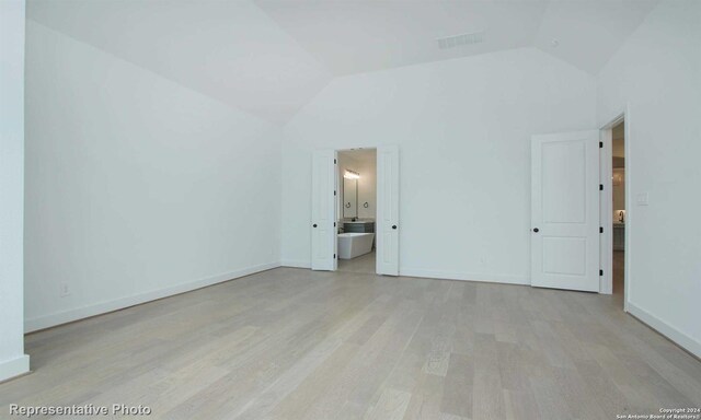 unfurnished bedroom with lofted ceiling, connected bathroom, and light hardwood / wood-style flooring