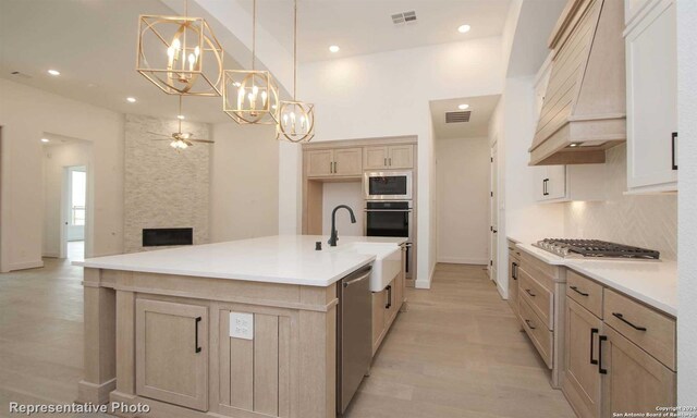 kitchen with pendant lighting, premium range hood, appliances with stainless steel finishes, backsplash, and a center island with sink