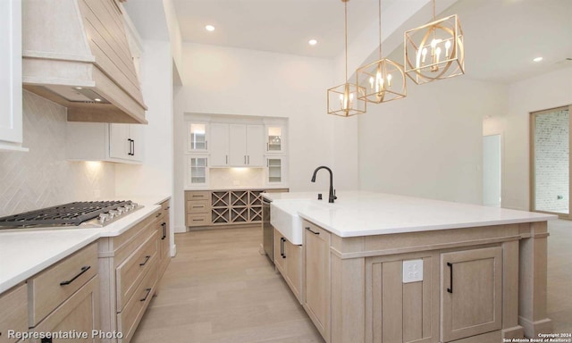 kitchen with sink, hanging light fixtures, a center island with sink, custom range hood, and stainless steel gas stovetop