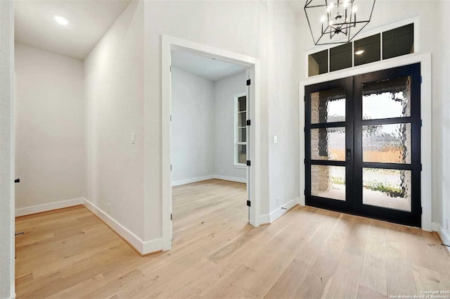 foyer entrance with french doors, an inviting chandelier, and light wood-type flooring