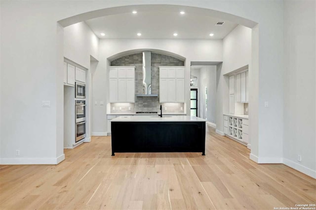 kitchen featuring light hardwood / wood-style flooring, stainless steel appliances, wall chimney exhaust hood, and a center island with sink