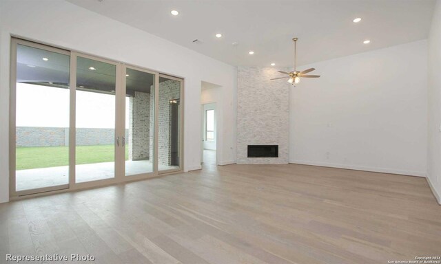 unfurnished living room with ceiling fan, a large fireplace, and light hardwood / wood-style floors