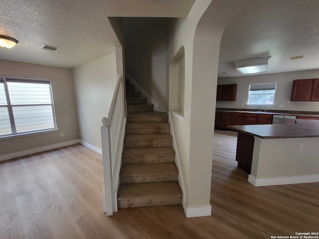 stairway with a wealth of natural light, a textured ceiling, and hardwood / wood-style flooring