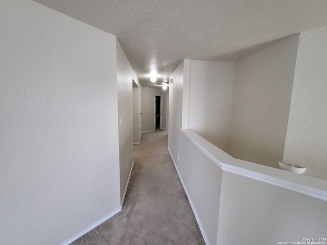 corridor featuring a textured ceiling and light carpet