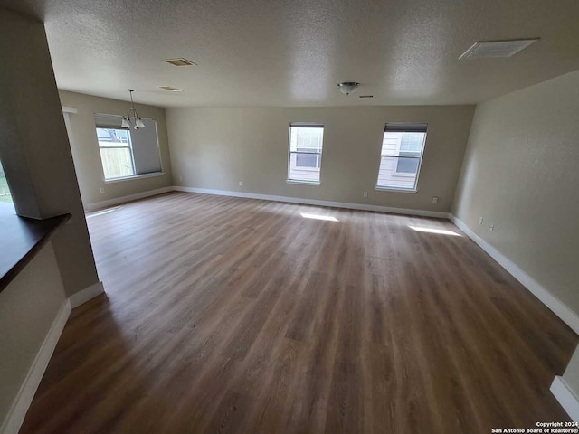 empty room featuring a textured ceiling, a healthy amount of sunlight, and dark hardwood / wood-style flooring