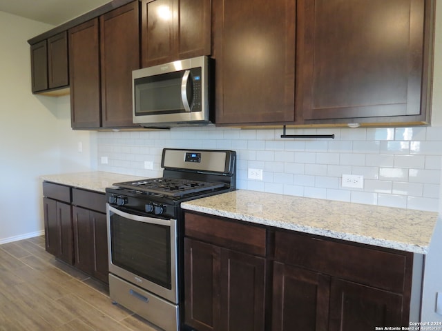 kitchen featuring appliances with stainless steel finishes, backsplash, light hardwood / wood-style floors, and light stone counters