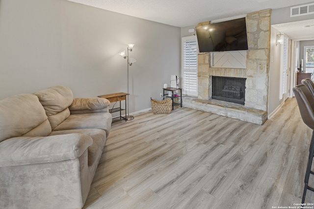 living room featuring a stone fireplace, a textured ceiling, and light hardwood / wood-style floors