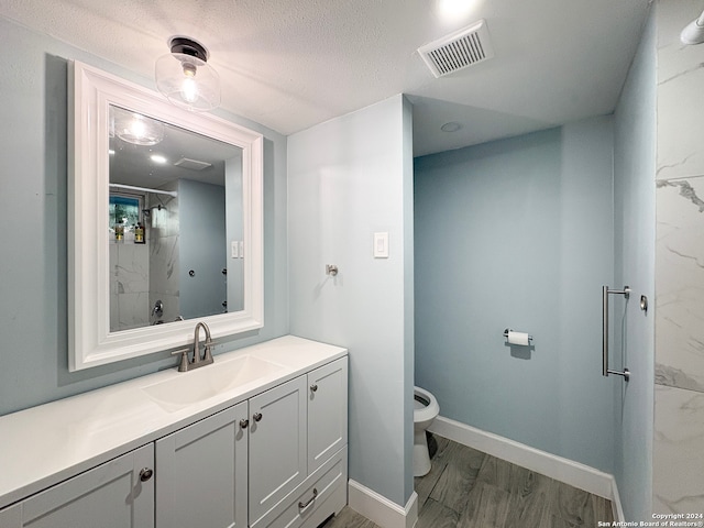 bathroom featuring wood-type flooring, a textured ceiling, an enclosed shower, vanity, and toilet