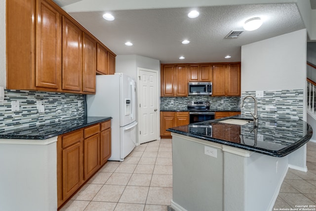 kitchen featuring dark stone counters, sink, kitchen peninsula, stainless steel appliances, and backsplash