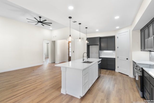 kitchen featuring appliances with stainless steel finishes, decorative backsplash, light wood-type flooring, a center island with sink, and sink