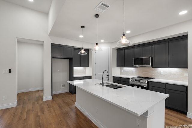 kitchen featuring appliances with stainless steel finishes, a center island with sink, sink, and light stone counters