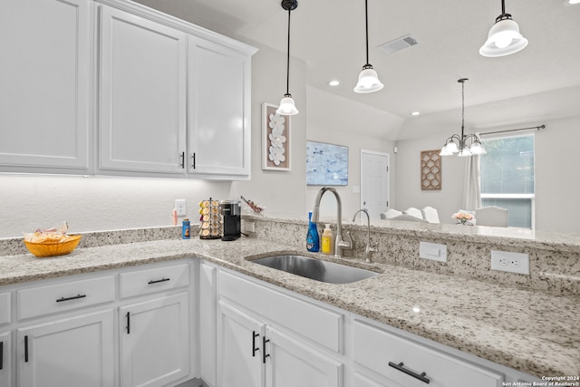 kitchen with pendant lighting, sink, white cabinetry, light stone countertops, and vaulted ceiling