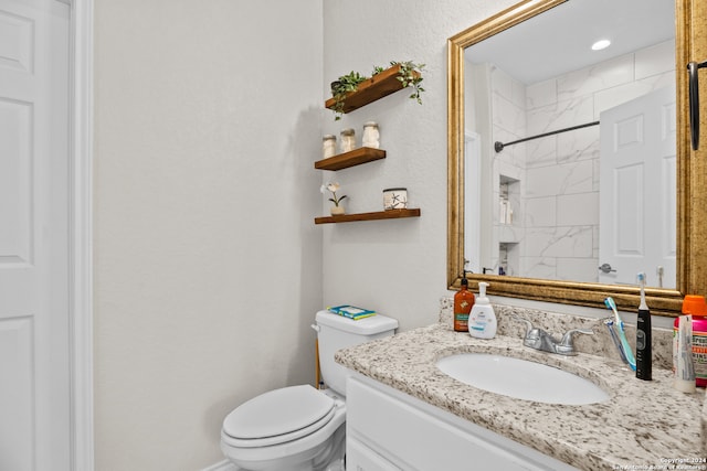 bathroom with a tile shower, vanity, and toilet