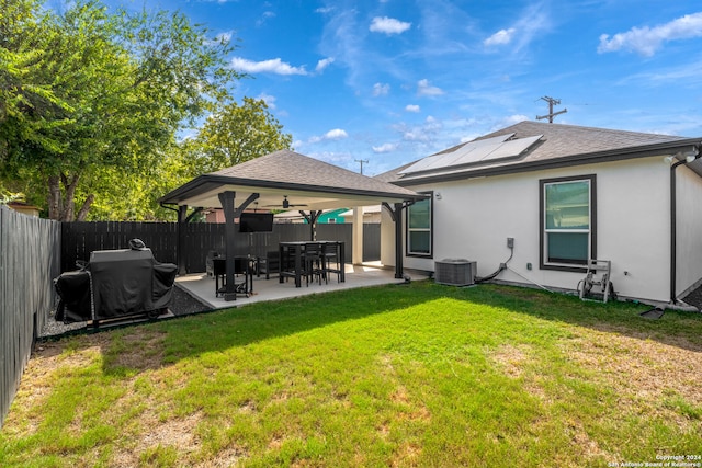 rear view of house with ceiling fan, cooling unit, a patio area, a yard, and solar panels