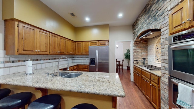 kitchen featuring a kitchen breakfast bar, kitchen peninsula, stainless steel appliances, light wood-type flooring, and sink