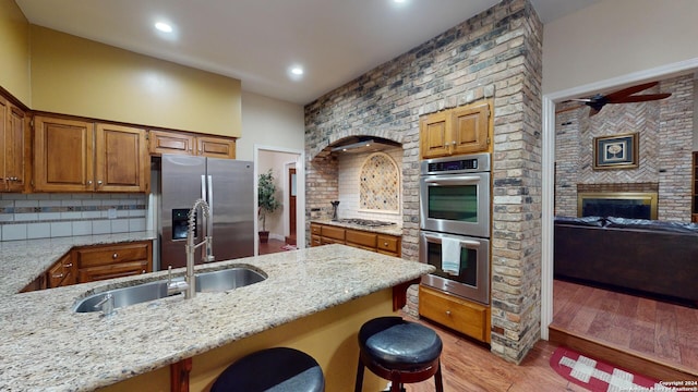 kitchen featuring appliances with stainless steel finishes, decorative backsplash, light hardwood / wood-style floors, light stone countertops, and a breakfast bar area