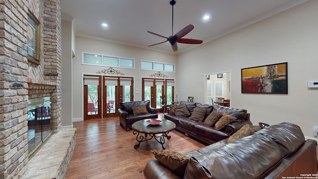 living room with ornamental molding, french doors, a fireplace, a towering ceiling, and light hardwood / wood-style floors