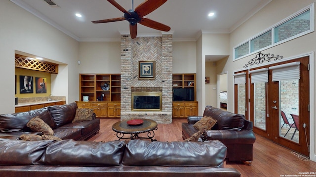 living room featuring a high ceiling, a fireplace, ornamental molding, and hardwood / wood-style floors