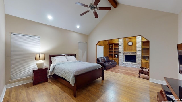 bedroom with beam ceiling, high vaulted ceiling, hardwood / wood-style floors, a large fireplace, and ceiling fan