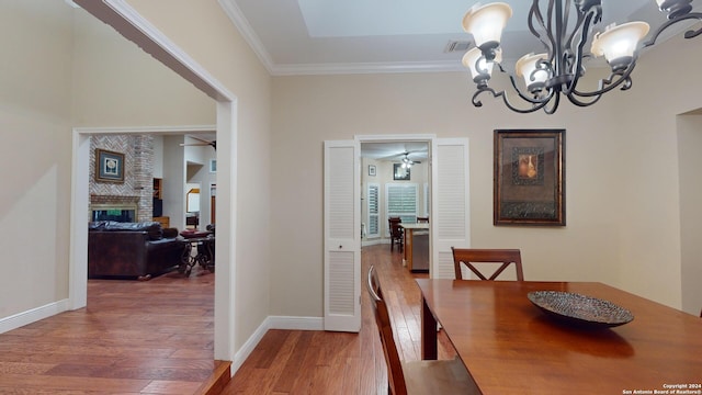 dining room with wood-type flooring, ceiling fan with notable chandelier, a brick fireplace, and ornamental molding