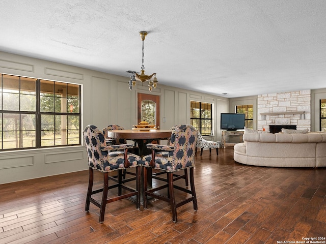 dining area featuring a stone fireplace, an inviting chandelier, dark wood-type flooring, and a textured ceiling