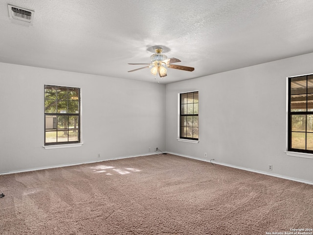 carpeted empty room with ceiling fan, a textured ceiling, and a healthy amount of sunlight