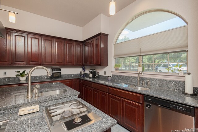 kitchen featuring stainless steel dishwasher, sink, decorative light fixtures, and dark stone counters