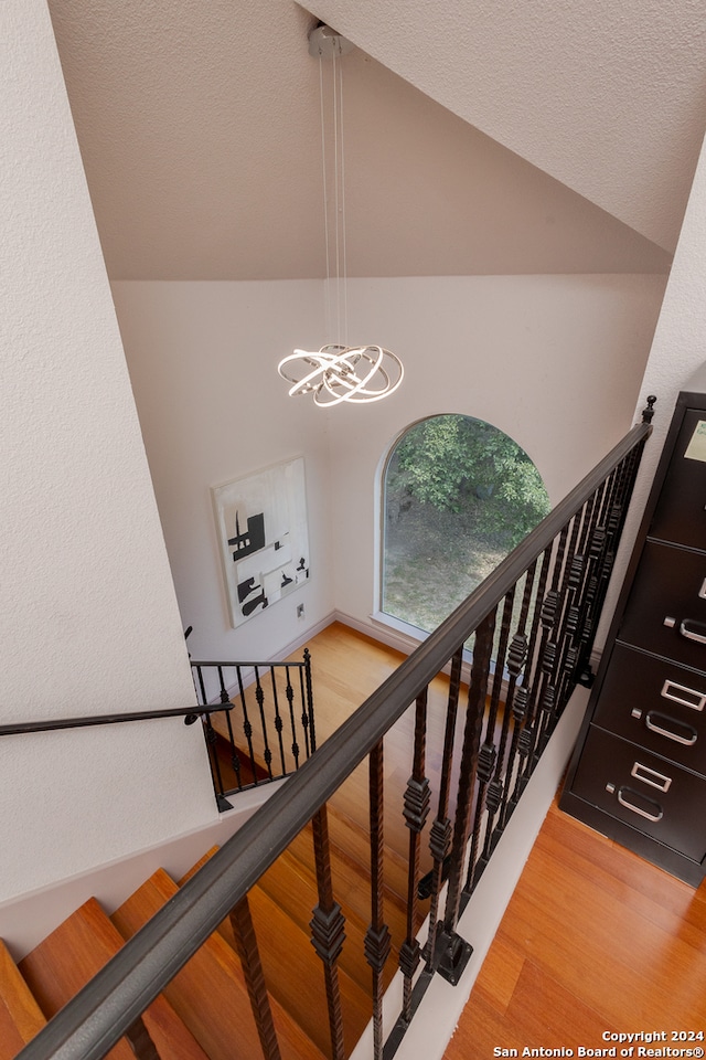 stairway featuring a notable chandelier, wood-type flooring, and lofted ceiling