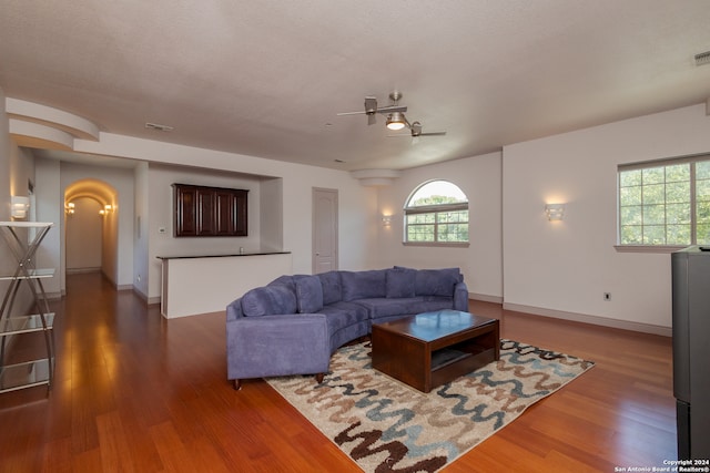 living room featuring dark wood-type flooring, ceiling fan, and a textured ceiling