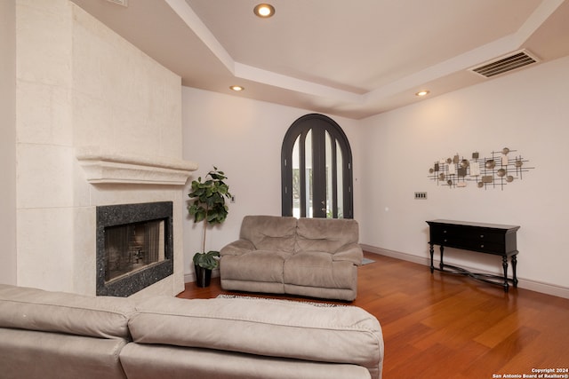 living room featuring hardwood / wood-style floors, a tiled fireplace, and a raised ceiling