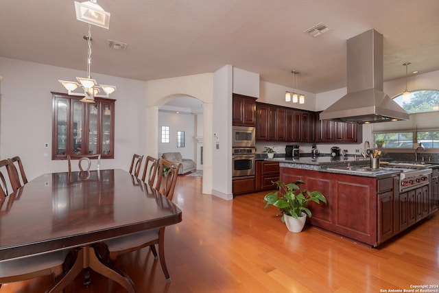 kitchen with appliances with stainless steel finishes, light hardwood / wood-style floors, island range hood, and pendant lighting